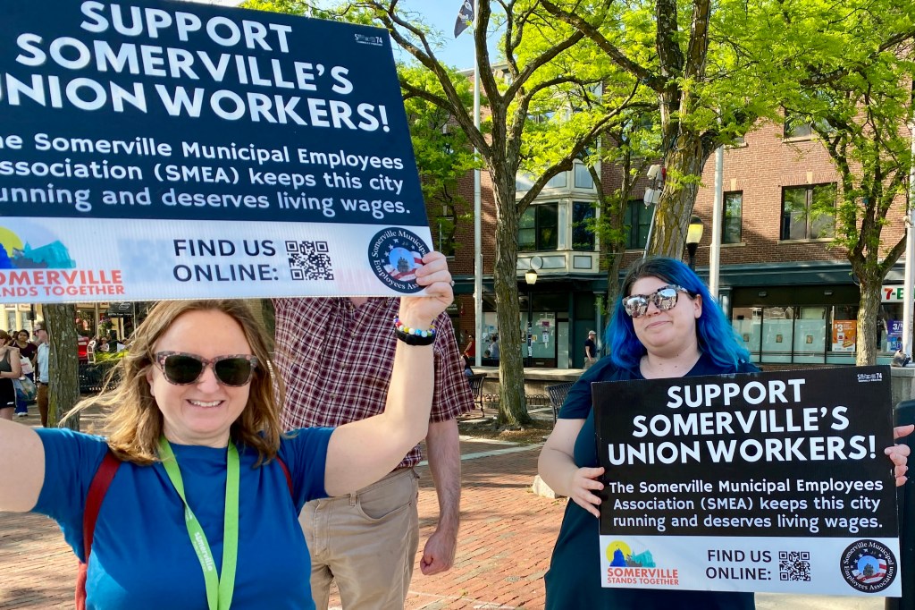 Two people hold "Support Somerville's Union Workers?" signs in Davis Square at a May 22, 2024, stand out.